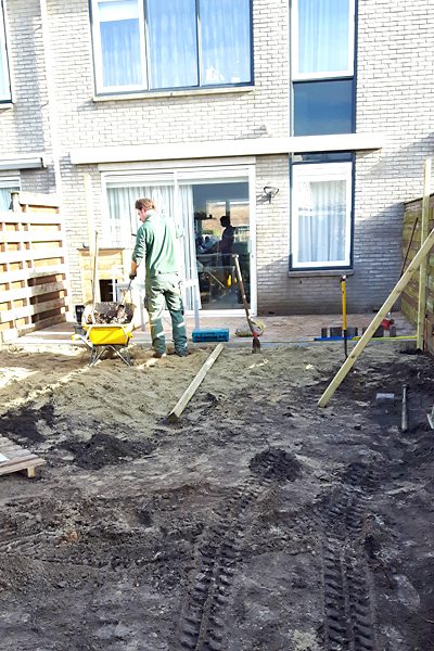 Hovenier egaliseert met een kruiwagen het zandbed voor nieuwe bestrating achter een woning