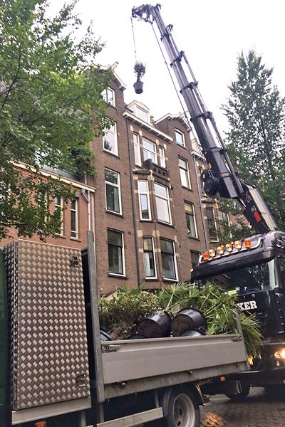 Kraanwagen hijst plantenbakken naar een dakterras van een Amsterdams grachtenpand