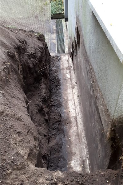 Diepe sleuf langs de fundering van een gebouw, klaar voor verdere werkzaamheden