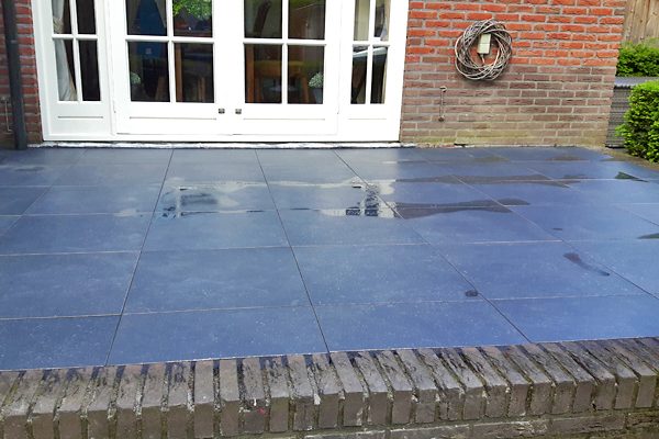 Afgerond terras van donkere natuursteentegels voor openslaande tuindeuren
