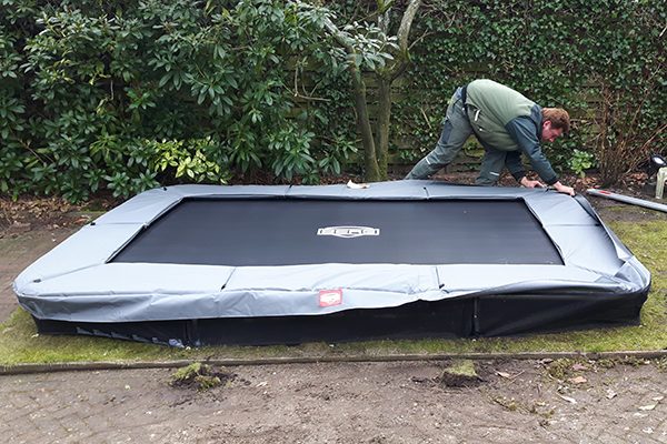 Medewerker plaatst een verdiepte trampoline in de uitgegraven kuil